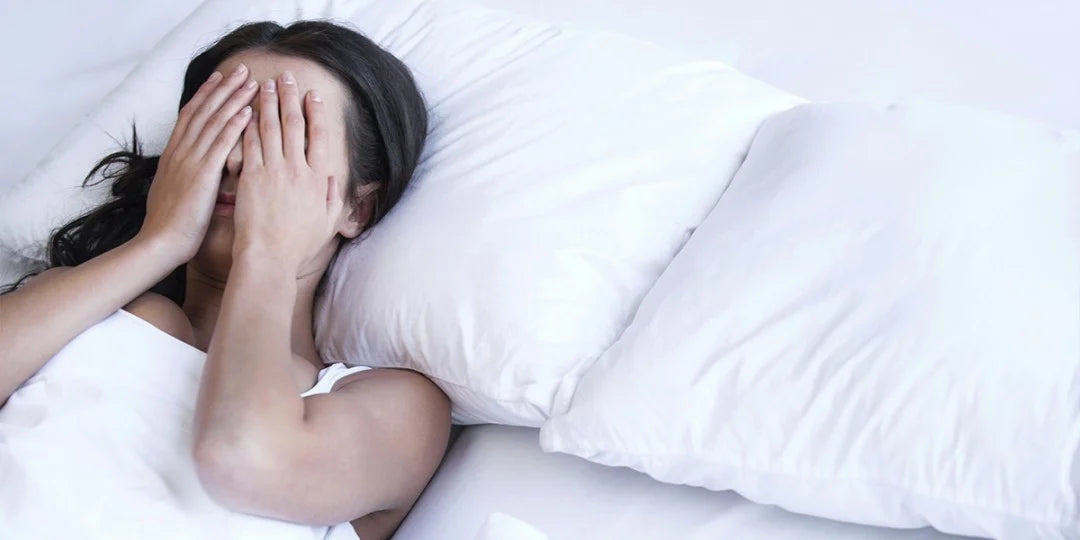 Person lying in bed with head in hands, possibly experiencing stress.