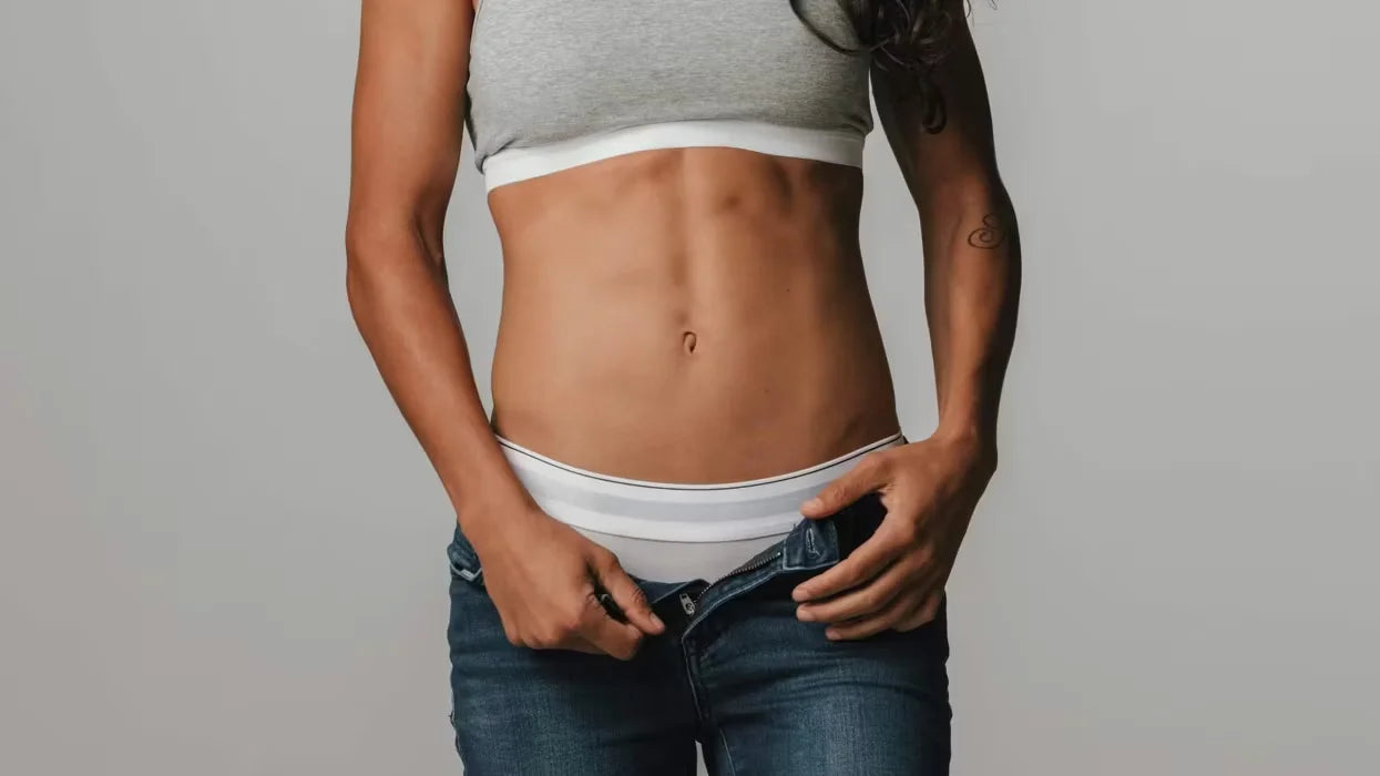 Person wearing a gray tank top and white underwear with blue jeans, holding the waistband.