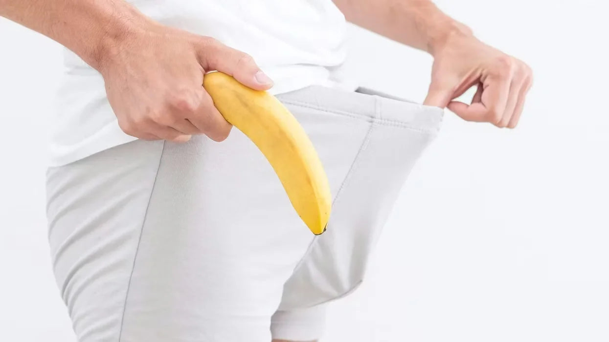 Person holding a banana behind their back with white pants.